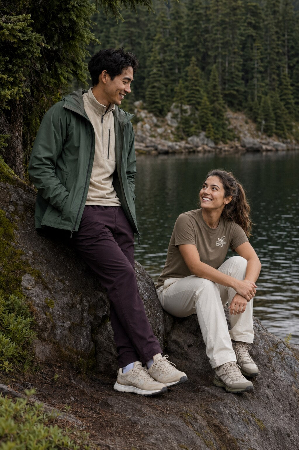 Friends in Live Longer clothing resting beside an alpine lake after a hike