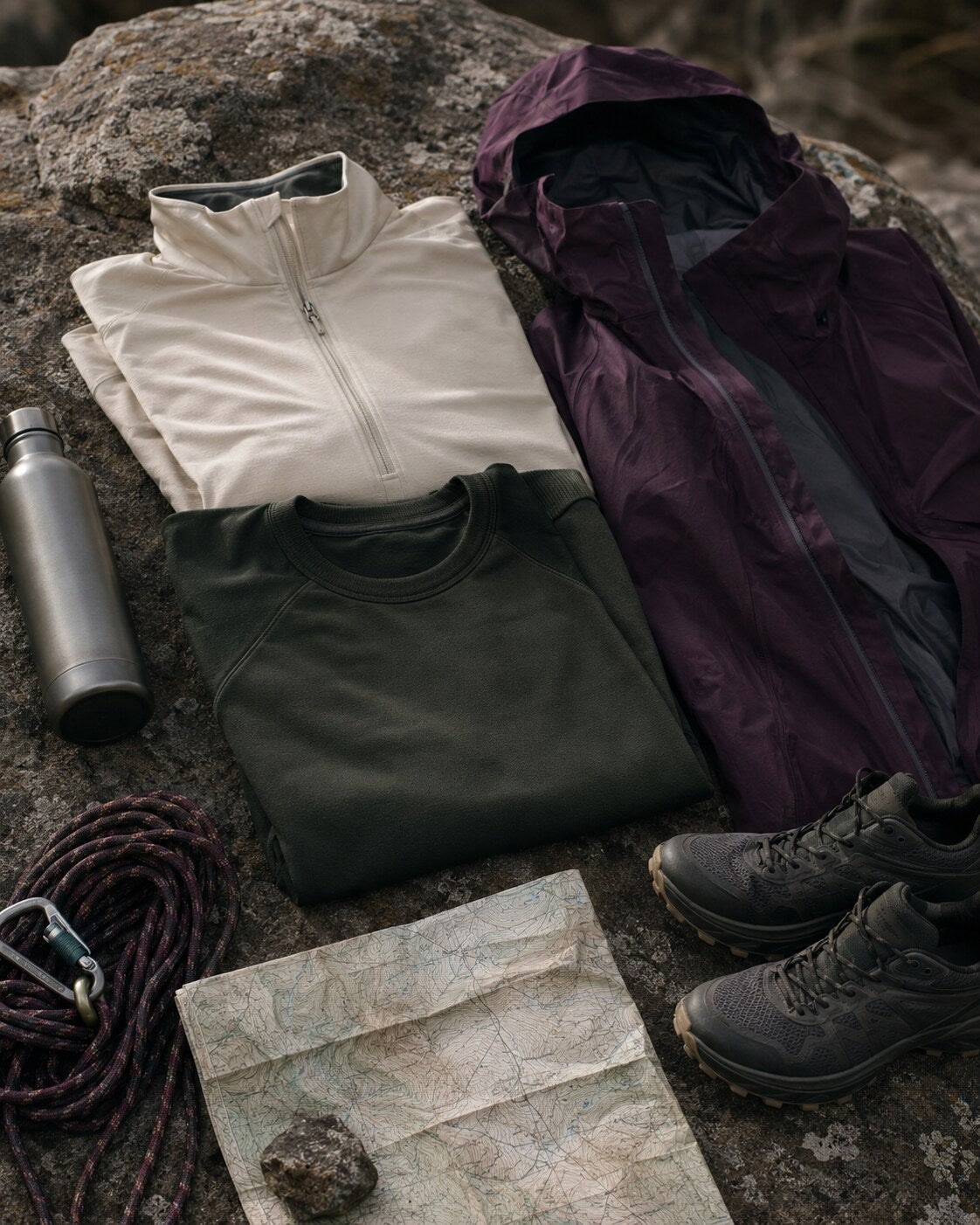 Outdoor clothing and trail essentials arranged on stone