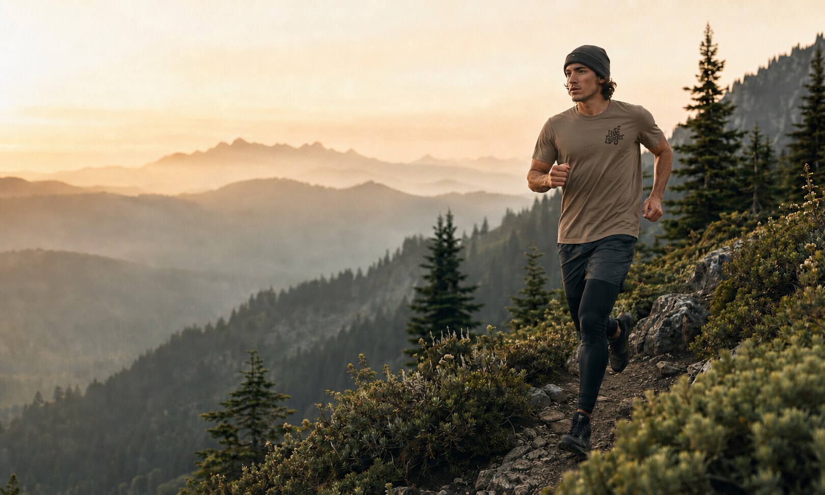 Runner wearing a taupe Live Longer T-shirt on an evergreen mountain trail at sunrise
